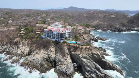 Orbit-with-pull-back-above-ocean-with-view-of-cliff-and-small-hotel-in-Oaxaca,-Mexico