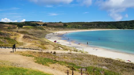 Panorama-shot-of-beautiful-Maitai-Bay-with-sandy-beach-and-relaxing-people-during-sunny-day-in-New-Zealand---Crystal-Clear-water-and-green-landscape