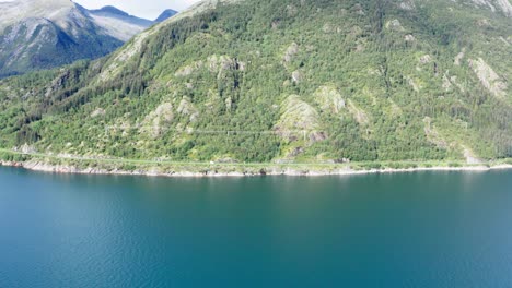 Aerial-View-Of-Scenic-Route-Of-Helgelandskysten-On-Lush-Coastal-Mountain-With-Calm-Blue-Ocean-In-Norway