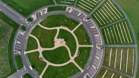 Circular-design-aerial-view-above-ornamental-landscaped-cemetery-garden-with-parking-around-outside-rising-rotate