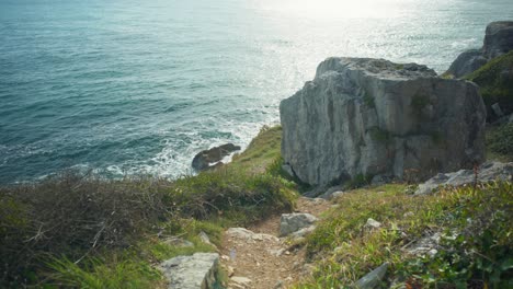 4K-Cinematic-shot-of-a-coastal-foot-path-going-down-hill-to-the-edge-of-a-cliff,-on-a-sunny-day,-on-the-island-of-Portland,-in-Dorset,-England
