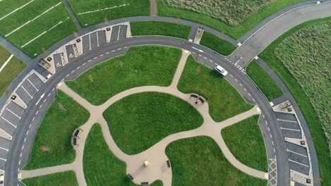 Circular-design-aerial-view-rotating-above-ornamental-landscaped-cemetery-garden-with-parking-around-outside