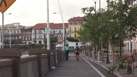 Two-men-walking-leisurely-along-the-scenic-coastal-promenade-of-the-Panama-Canal-at-Casco-Viejo,-Panama-City