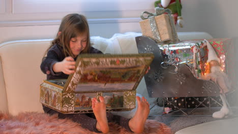 Surprised-and-Excited-young-girl-opening-Box-with-presents-in-front-of-Christmas-decoration-with-gifts-and-packages-on-santa-sledge