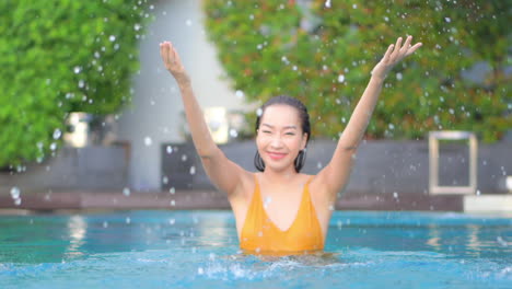 Happy-Asian-Woman-in-Swimsuit-Playing-and-Spraying-Water-in-Swimming-Pool-on-Hot-Summer-Day,-Slow-Motion