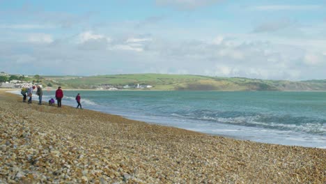 4K-Panoramic-landscape-panning-shot-of-Weymouth's-beach-sea-front-on-a-sunny-day,-with-a-family-playing-and-throwing-stones-into-the-ocean
