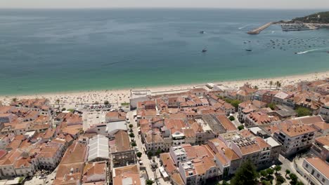 Antenne-Rückwärts-Aufsteigend-über-Die-Küstenstadt-Sesimbra-Mit-Hafen-Im-Hintergrund,-Portugal