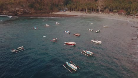 Drone-shot-flying-over-with-camera-tilting-down-over-fishermen-boat's-in-a-tropical-bay-at-sunset-on-Nusa-Penida,-Indonesia-in-4k