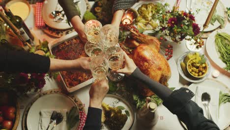 People-clink-their-glasses-with-white-wine-over-plated-and-decorated-thanksgiving-table-with-big-roasted-turkey-in-the-middle