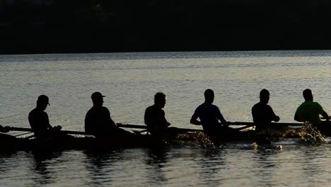 Equipo-De-Remo-Masculino-Atlético-Practicando-Carreras-De-Deportes-Acuáticos-En-El-Reflejo-Del-Agua-Del-Lago-Al-Atardecer