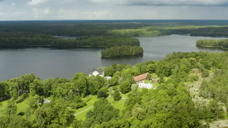 Aerial,-tilt-up,-drone-shot-away-from-the-Fagervik-manor,-lake-Bruntrasket-in-the-background,-partly-sunny,-summer-day,-in-Inkoo,-Uusimaa,-Finland