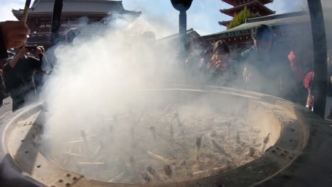 People-waving-in-the-smoke-of-an-Incense-Burner-At-A-Temple-In-Tokyo,-Japan