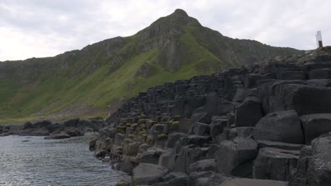 Impresionante-Paisaje-De-Las-Columnas-Hexagonales-De-Basalto-Entrelazadas-Con-Las-Verdes-Montañas-Costeras-Al-Fondo-En-La-Calzada-Del-Gigante-En-Irlanda-Del-Norte