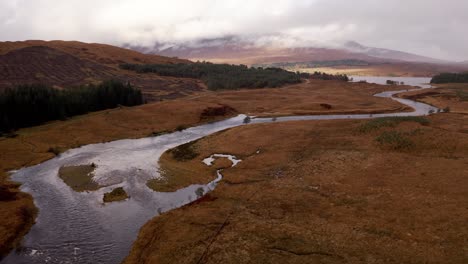 Blick-Auf-Einen-Fluss,-Der-Im-Schottischen-Hochland-In-Einen-See-Namens-Glencoe-Fließt,-Mit-Hügeln-Im-Nebel-Im-Hintergrund