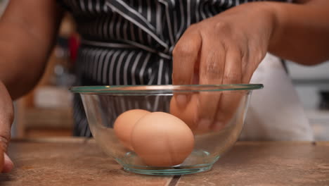 Cracking-four,-organic,-free-range,-brown-eggs-into-a-mixing-bowl---side-view-in-slow-motion