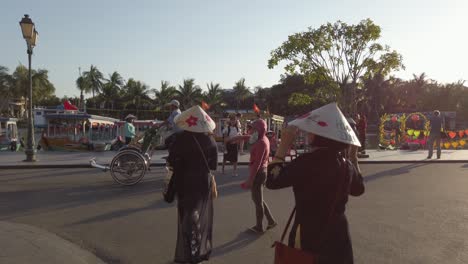 Dos-Mujeres-Con-Sombreros-De-Hojas-Caminando-Por-Las-Calles-Del-Pueblo-Con-Tráfico-De-Ciclobicicletas-Delante,-Siguen-Detrás-De-Tiro