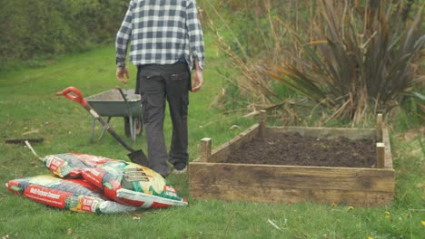 El-Joven-Jardinero-Lleva-Una-Bolsa-De-Abono-Y-Cae-Al-Lado-De-Una-Cama-De-Jardín-Elevada