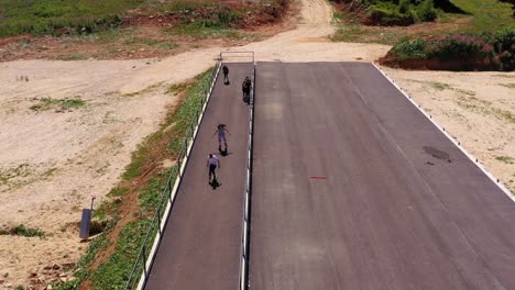 Niños-Corriendo-En-Patines-Durante-El-Verano-En-Una-Pista-De-Asfalto,-Toma-De-Seguimiento-Aérea