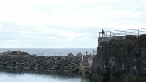 Static-tripod-shot-of-a-young-couple-standing-above-a-stone-pier-in-Seixal,-Portugal