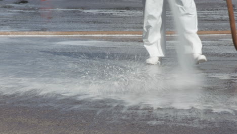 Brazilian-soldier-in-protective-gear-hosing-down-the-road-outside-of-a-hospital,-telephoto-shot-of-legs