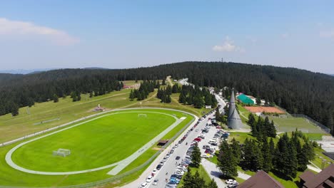 Campo-De-Fútbol-Del-Hotel-Rogla-Resort-Con-Iglesia-Podruznicna-A-La-Derecha-Durante-La-Temporada-De-Primavera,-Tiro-Aéreo