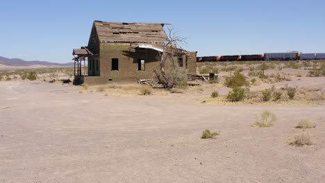 Freight-train-shipping-goods-through-the-desert-passes-a-dirt-road-crossing-and-a-dilapidated-abandoned-house