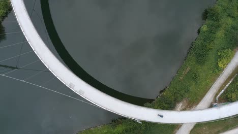 Aerial-top-down-static-view-of-lone-cyclist-crossing-curved-modern-bridge