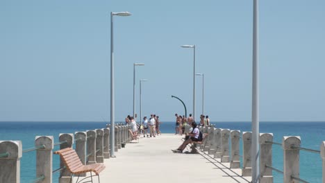 Summertime-scene-of-people-enjoying-Porto-Santo-island-pier,-relaxing-and-kids-playing-soccer-with-blue-ocean-sea-water-in-background,-Portugal,-static