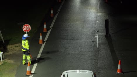 Verkehrswächter-Mit-Langsamem-Zeichen-Und-Geführtem-Verkehrsstab,-Der-Nachts-Fahrende-Autos-Leitet---Nsw-qld-grenze-Während-Covid-19---Goldküste,-Australien