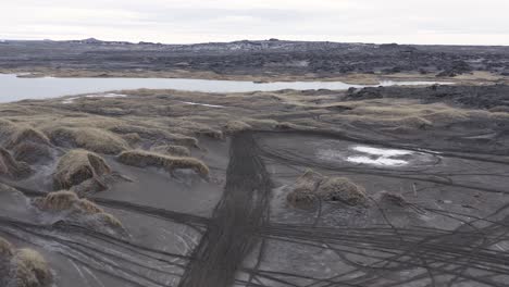 Lines-of-dirt-track-in-dunes-of-Sandvik-beach-in-Iceland,-aerial