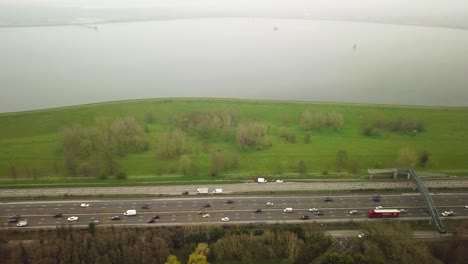 Drone-shot-view-of-busy-motorway-transport-in-nature-close-to-a-lake