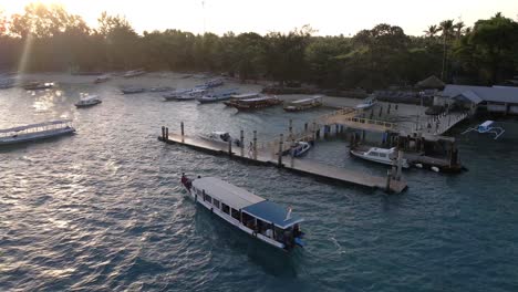 Barco-De-Viaje-Turístico-Que-Llega-Al-Muelle-En-La-Isla-De-Gili-Air-Durante-La-Puesta-De-Sol-En-Segundo-Plano