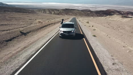 Toma-Aérea-De-Una-Turista-Que-Se-Inclina-Fuera-Del-Auto-En-El-Valle-De-La-Muerte,-Un-Hermoso-Destino-Para-Viajar