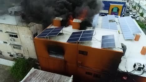 Aerial-view-of-a-smoking-building-with-solar-panels-burning---static,-drone-shot