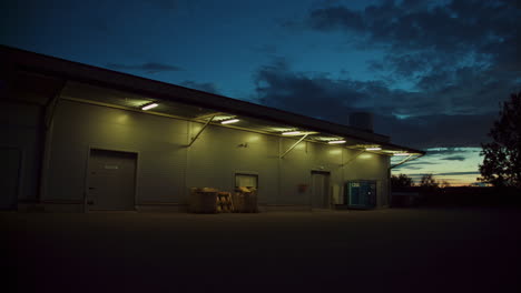 Vista-Exterior-De-Un-Edificio-De-Almacén-De-Acero-Iluminado-Durante-El-Anochecer