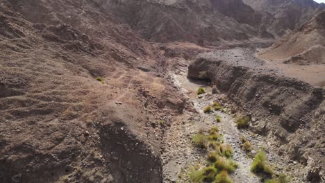 Flying-over-a-dry-arid-wadi-valley-looking-down-at-the-dry-riverbed-and-tilting-up-to-look-at-surrounding-mountains
