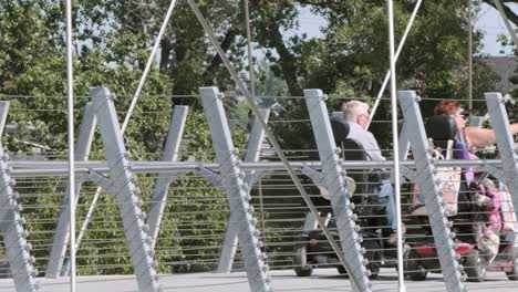 Elderly-couple-ride-scooters-across-foreshortened-Calgary-foot-bridge