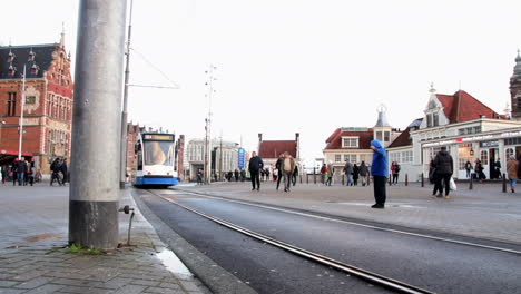 People-Walking-And-Tram-Passing-By-The-Amsterdam-Centraal-Railway-Station-In-Amsterdam,-The-Netherlands-At-Daytime---ground-level,-static-shot