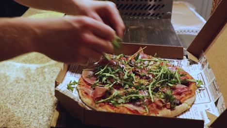 A-pizza-chef-adds-rocket,-arugula,-to-the-top-of-a-freshly-baked-pizza-before-sending-it-out-for-delivery