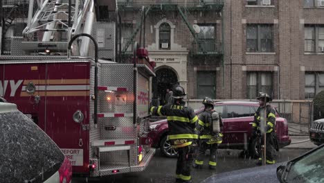 Firemen-stand-by-extended-firetruck-ladder-under-snowfall---Wide-Tilt-down-shot