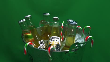 2-2-Zweisprachig-Französisch-Englisch-Corona-Extra-Coronita-6-Packung-Glasflaschen-In-Eiskübel-Mit-Hängenden-Zuckerstangen,-Die-Sich-Vor-Einem-Grünen-Bildschirm-Drehen,-Um-Die-Festliche-Weihnachtszeit-Des-Friedens-Zu-Feiern