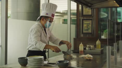 Jefe-De-Cocina-Con-Máscara-Y-Protector-Facial-Mezclando-Plato-De-Arroz-En-La-Plancha-En-El-Restaurante-Durante-La-Pandemia