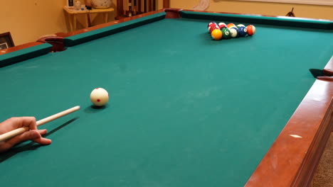 Person-Breaks-Pool-Balls-on-8-Ball-Triangle-Rack-on-the-Spot-with-Solid-and-Stripped-Billiard-Balls-Scattering-Across-Brunswick-Table-with-wooden-Cue-Stick-on-Green-Felt-or-Cloth,-no-faces,-wide-angle
