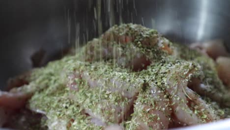 Pouring-Dry-Herbs-On-Freshly-Cut-Chicken-Meat-In-A-Stainless-Basin