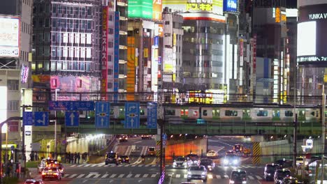 Erhöhte-Nachtansicht-Mit-Blick-Auf-Verkehr,-Kreuzungen-Und-Jr-züge,-Die-über-Eine-Brücke-Fahren,-Mit-Kabukicho-Im-Hintergrund,-In-Shinjuku,-Tokio