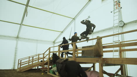 Stuntman-with-ax-jumps-off-horse-to-attack-actors-on-rehearsal-platform,-Slowmo