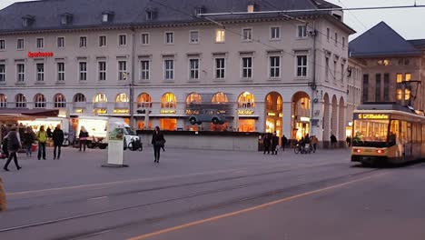 Straßenbahn,-Die-Am-Marktplatz-In-Karlsruhe-Vorbeifährt,-Mit-Einer-Anzeige-Von-Volkswagen,-Die-In-Einer-Metallstruktur-Hängt