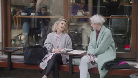 Two-Caucasian-Women-Talking-While-Sitting-Outside-A-Cafeteria-In-Tokyo,-Japan-On-A-Fine-Weather