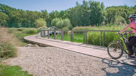 Two-cyclists-with-helmets-riding-their-mountain-bike-crossing-a-wooden-brown-bridge