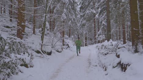 Tall-and-athletic-man-in-green-neon-outfit-running-in-frosty-pine-forest-on-snowy-path-on-cold-winter-day---toward,-slow-motion